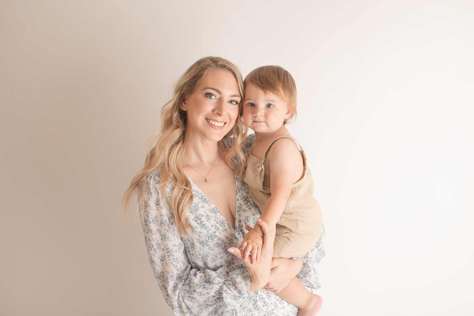 A smiling mother holds her toddler in her arms while standing in a studio in a blue dress before visiting Pittsburgh birthday parties for kids