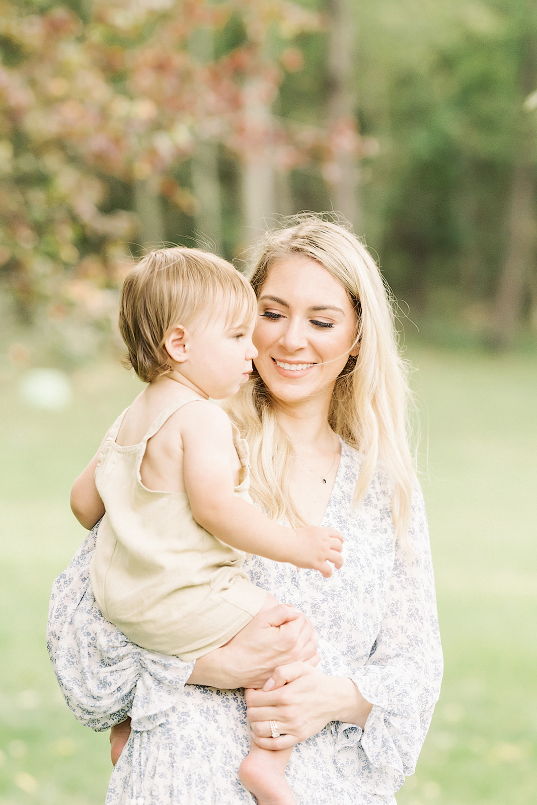 A happy mother walks through a park with her toddler son on her hip