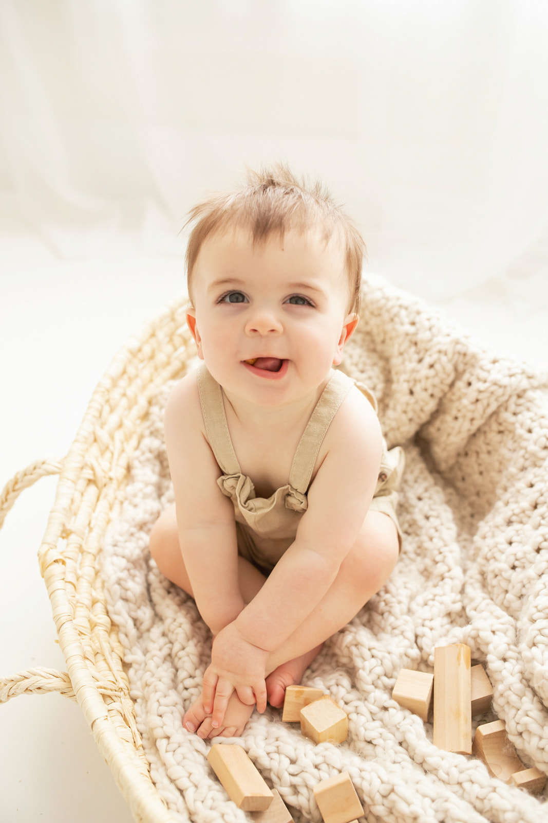 A toddler boy sits in a basket playing with wooden blocks on the floor of a studio before visiting Pittsburgh splash pads