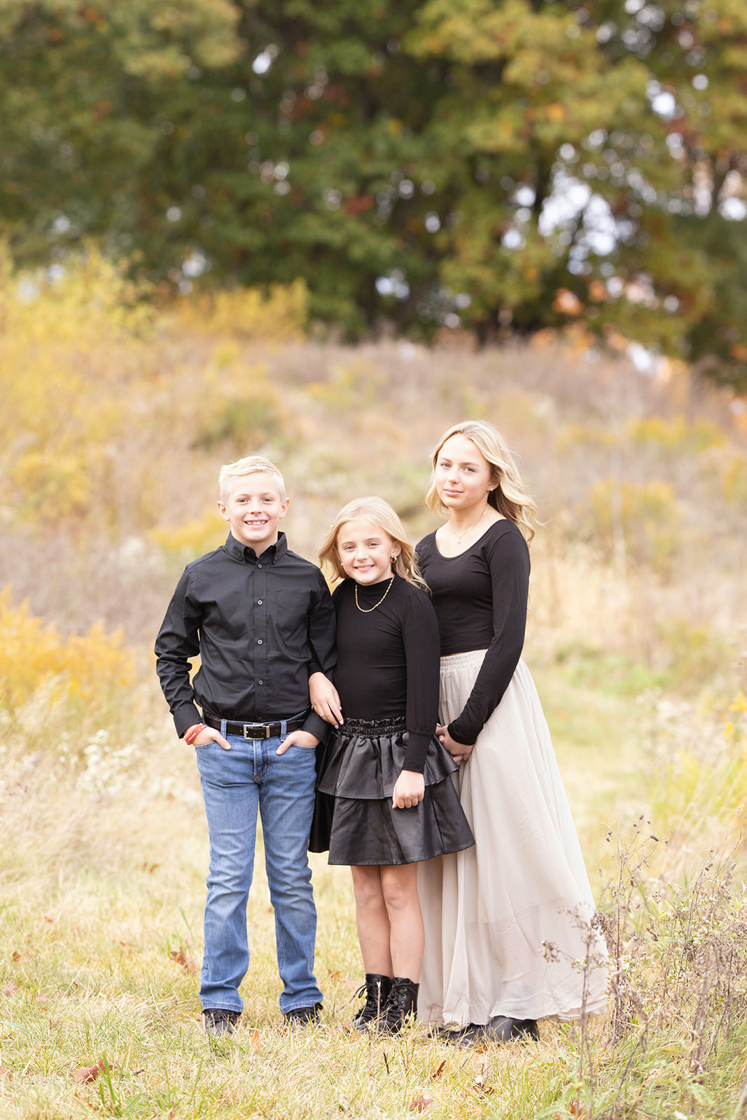 Three young siblings stand together in a field of tall grass in black tops before finding Pittsburgh summer camps