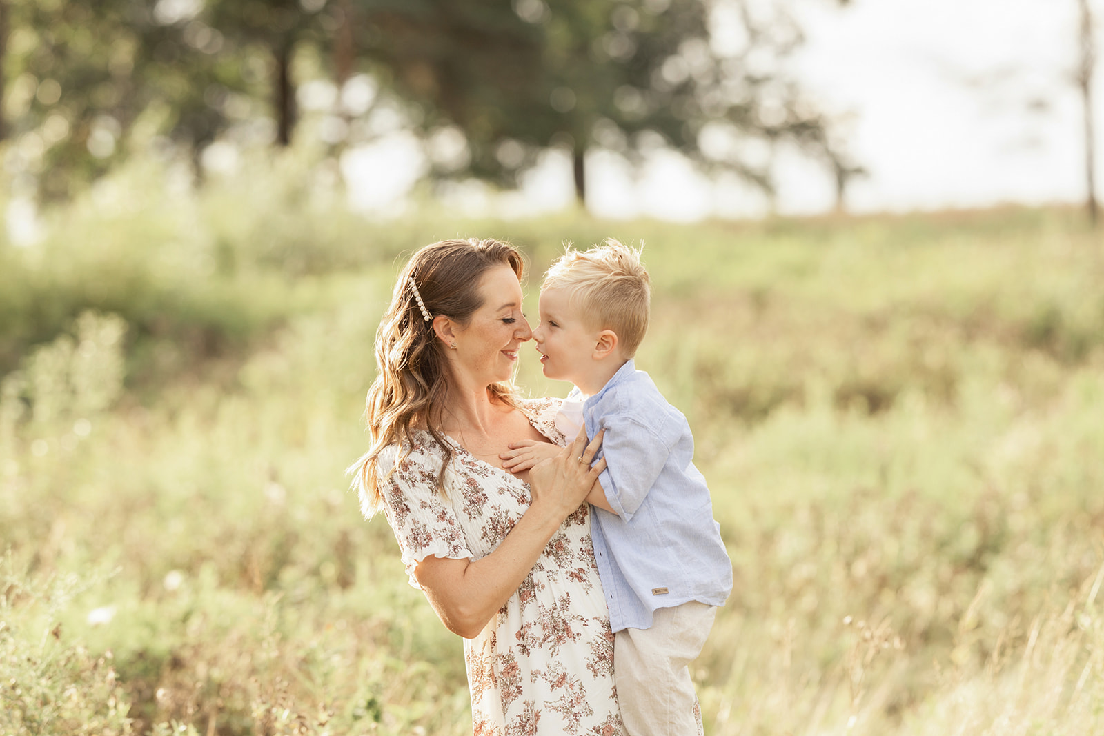 A toddler boy touches noses with his mom while they play in a field of tall grass at sunset before some Pittsburgh Swimming Lessons