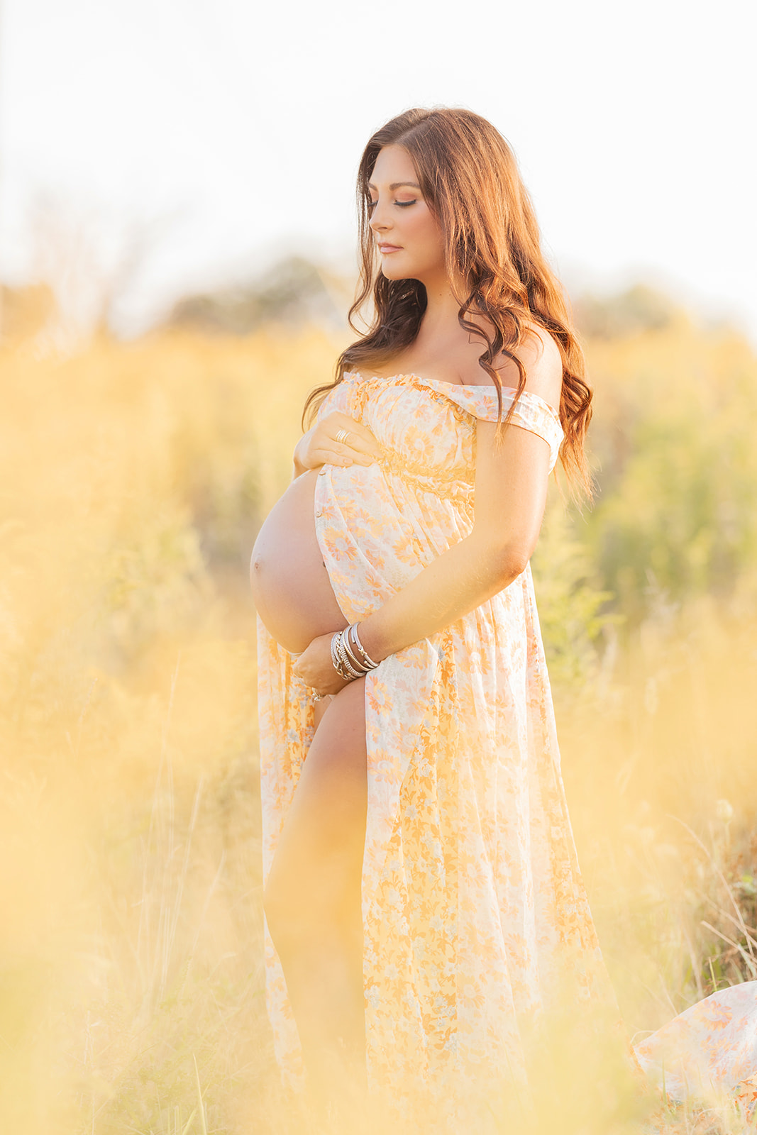 A mom to be stands in a field of tall grass in an open front yellow maternity dress with eyes closed before visiting Pittsburgh yoga studios