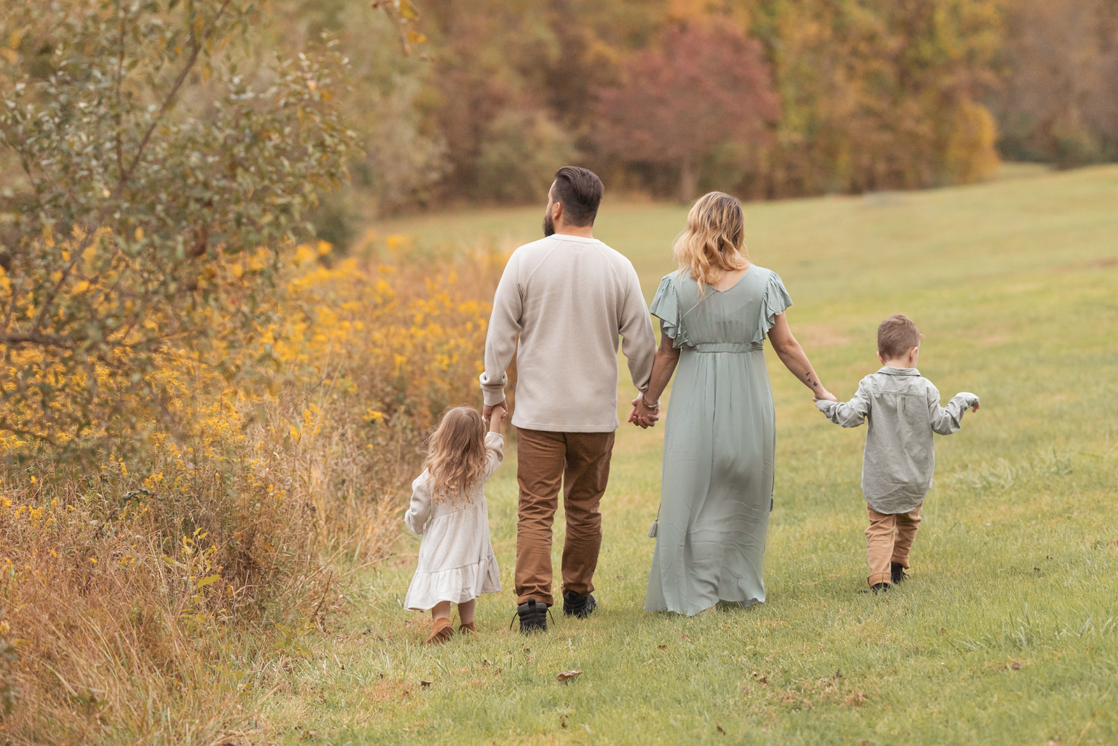 A mom and dad walk in a park in fall holding hands with their toddler son and daughter on each side before visiting private schools Pittsburgh