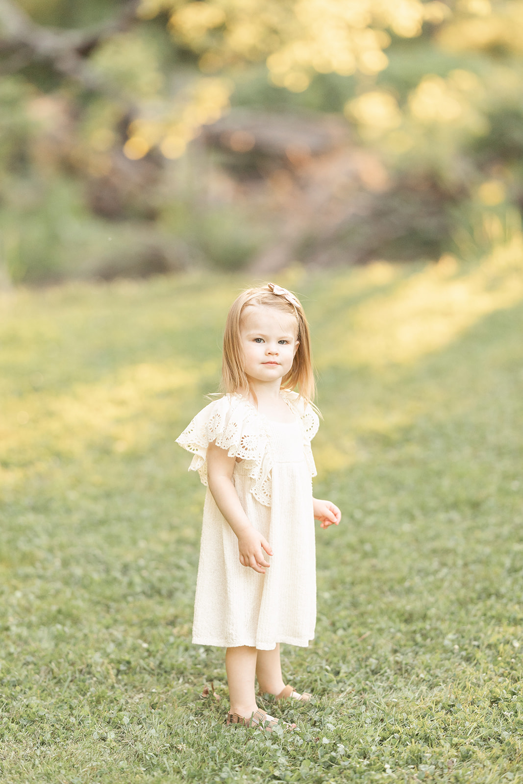 A toddler girl in a white dress explores a grassy park during things to do in Pittsburgh with kids