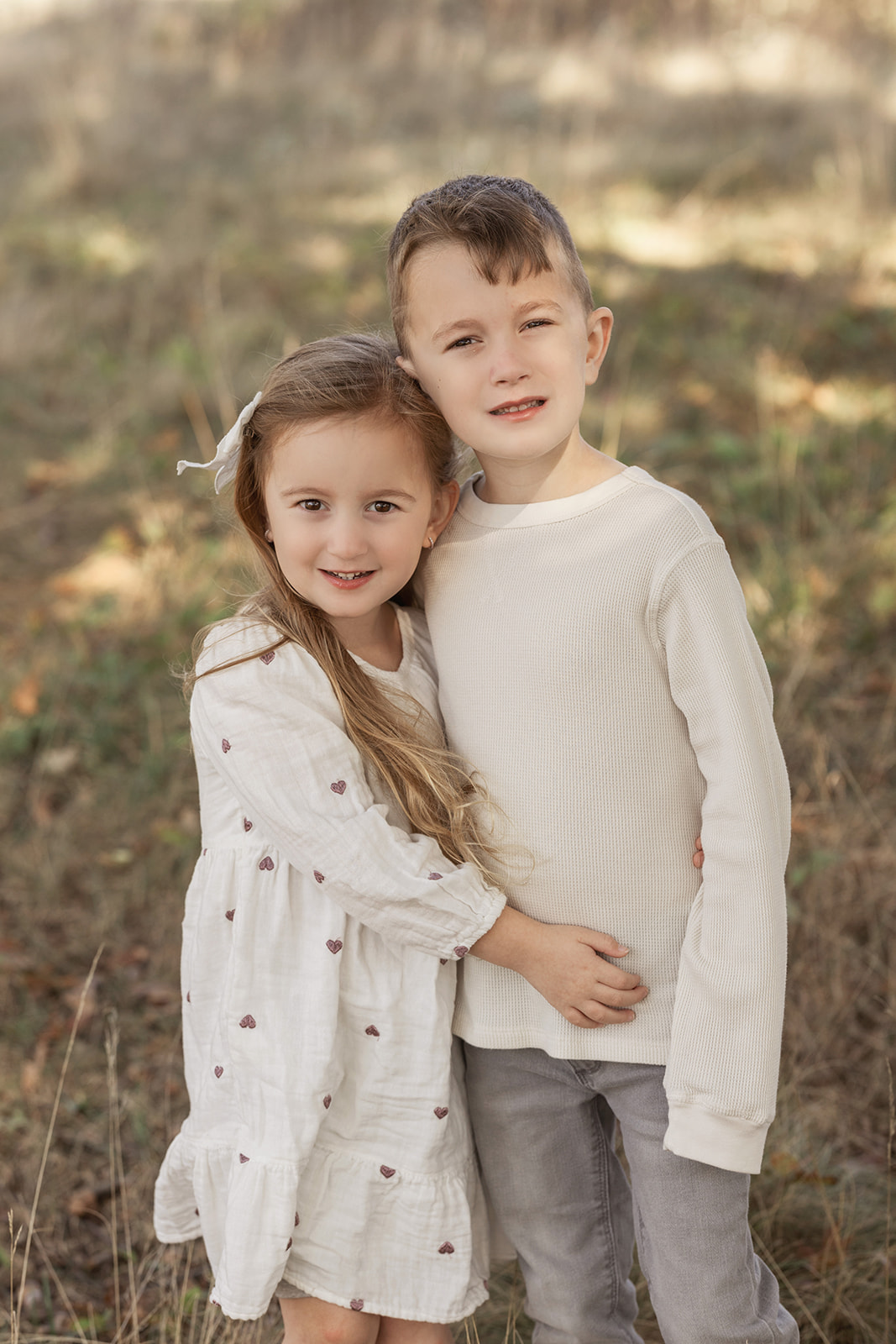 Toddler brother and sister in white hug while standing in a park before visiting Christmas Lights in Pittsburgh