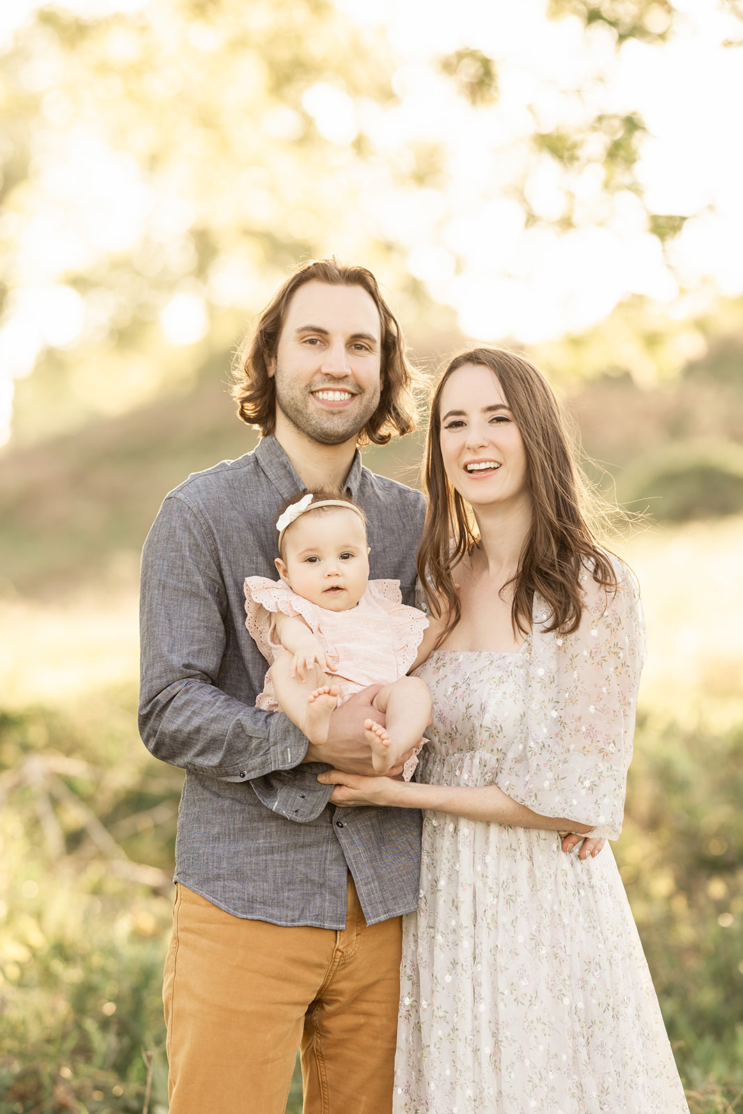 Happy new parents smile in a park at sunset with their baby daughter in their hands before exploring Pittsburgh Christmas Tree Farms