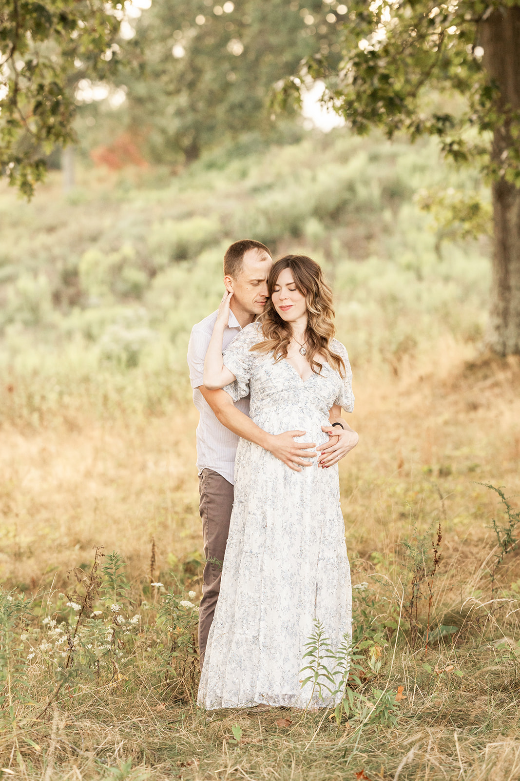 A happy expecting couple snuggle under a tree after visiting All About Women Weirton, WV