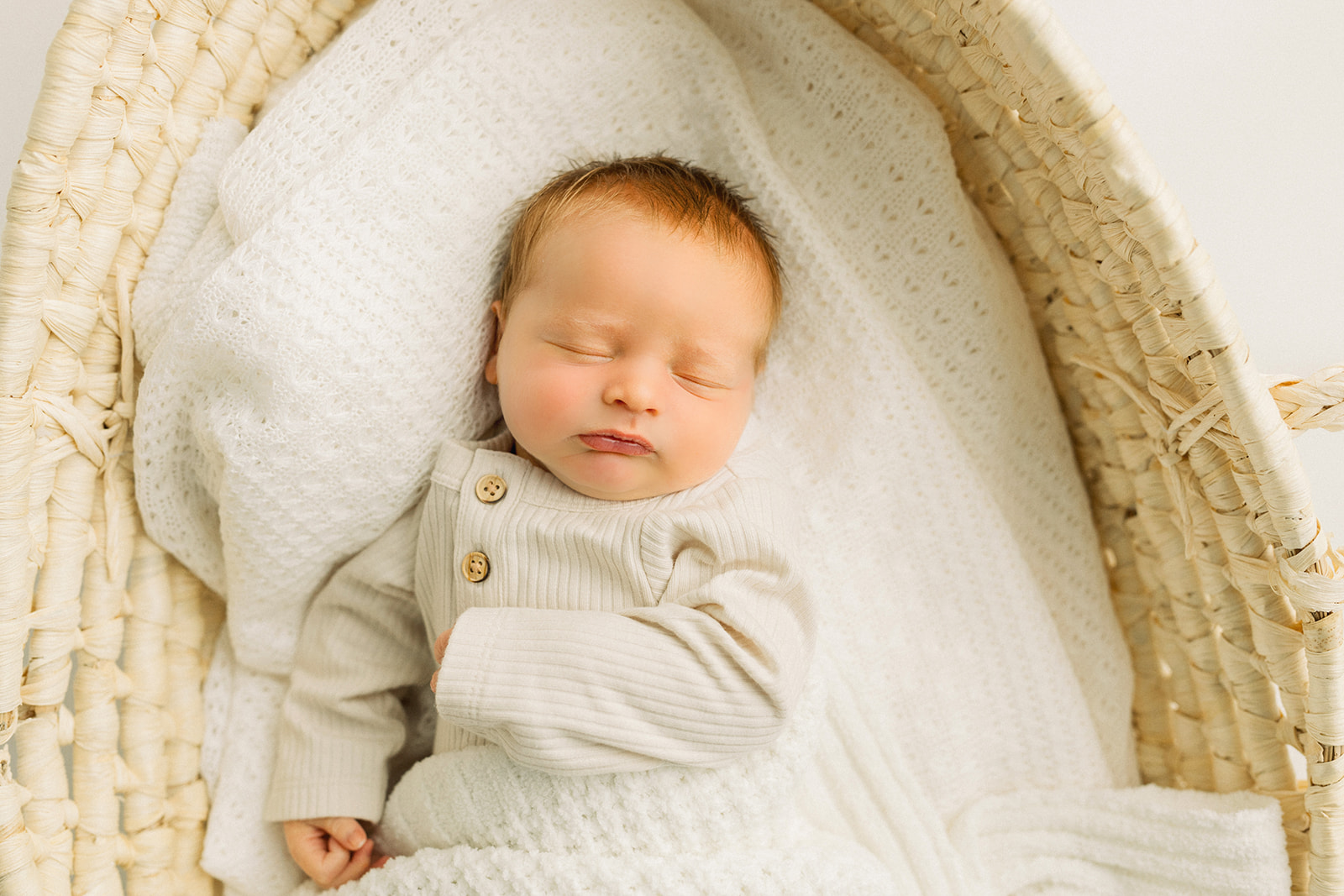 A newborn abby sleeps in a woven basket and tan onesie