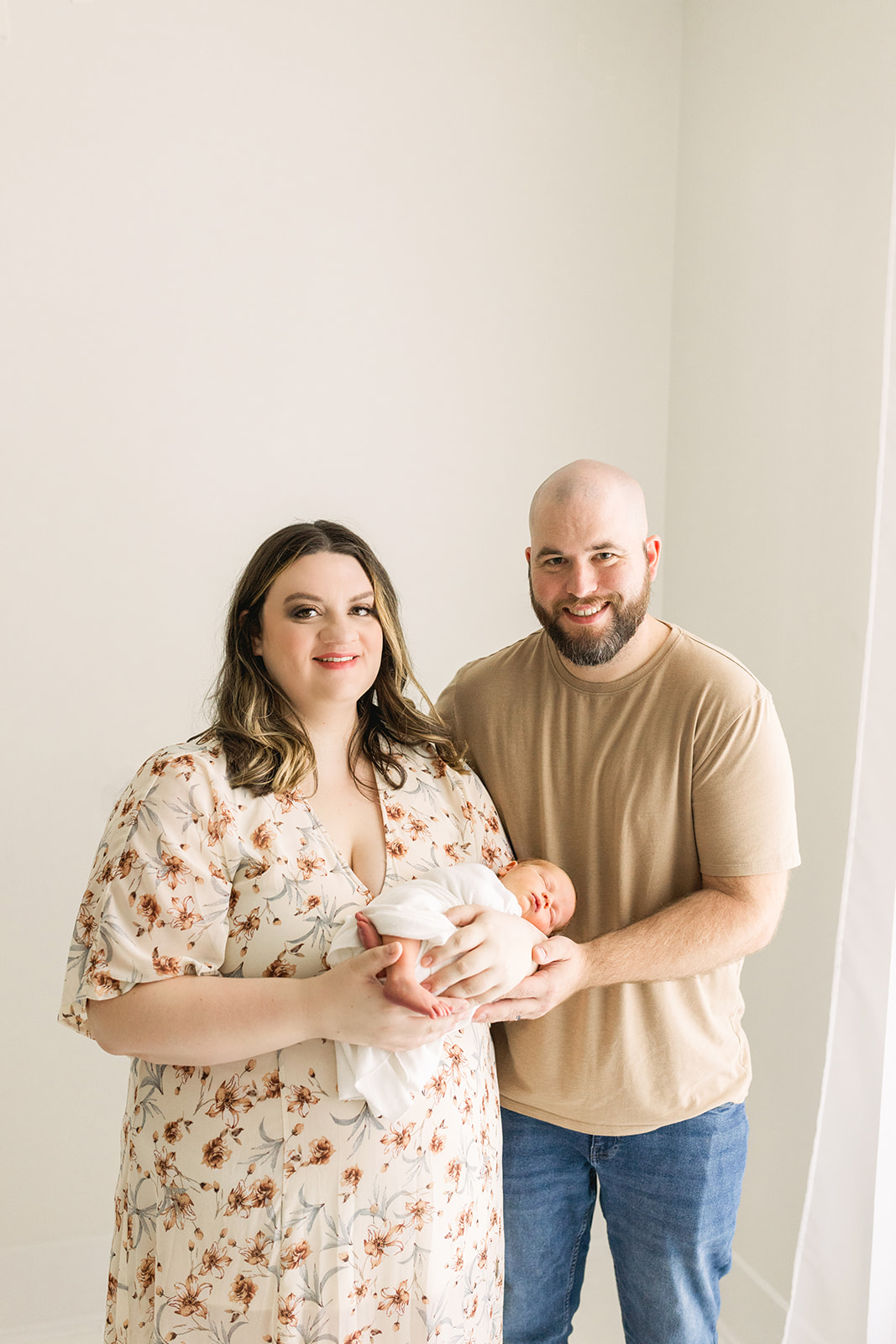 Happy new parents smile in a studio holding their sleeping newborn after visiting baby stores in Morgantown, WV