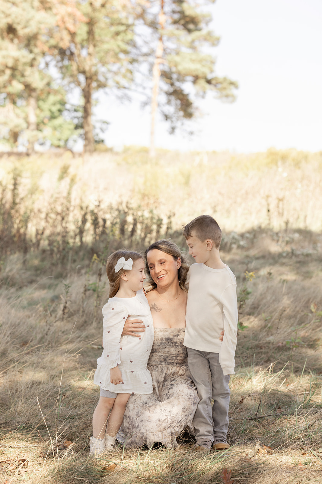 A happy mom kneels in a field of tall grass hugging her toddler son and daughter before some holiday events in Pittsburgh