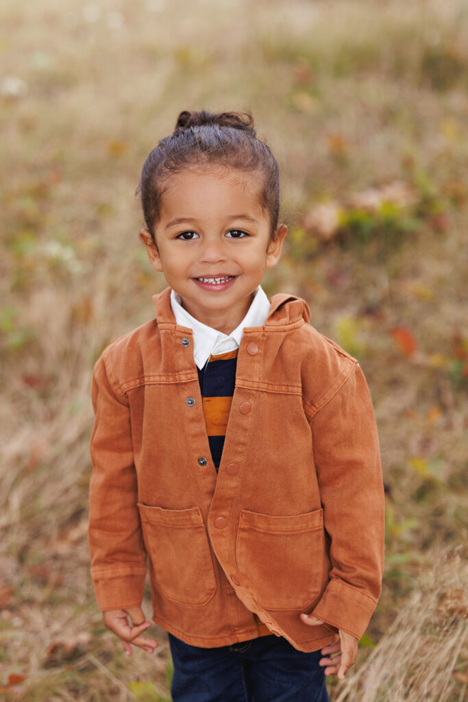 A toddler girl in an orange jacket smiles while exploring a park at sunset after visiting birthday party places in Morgantown, WV