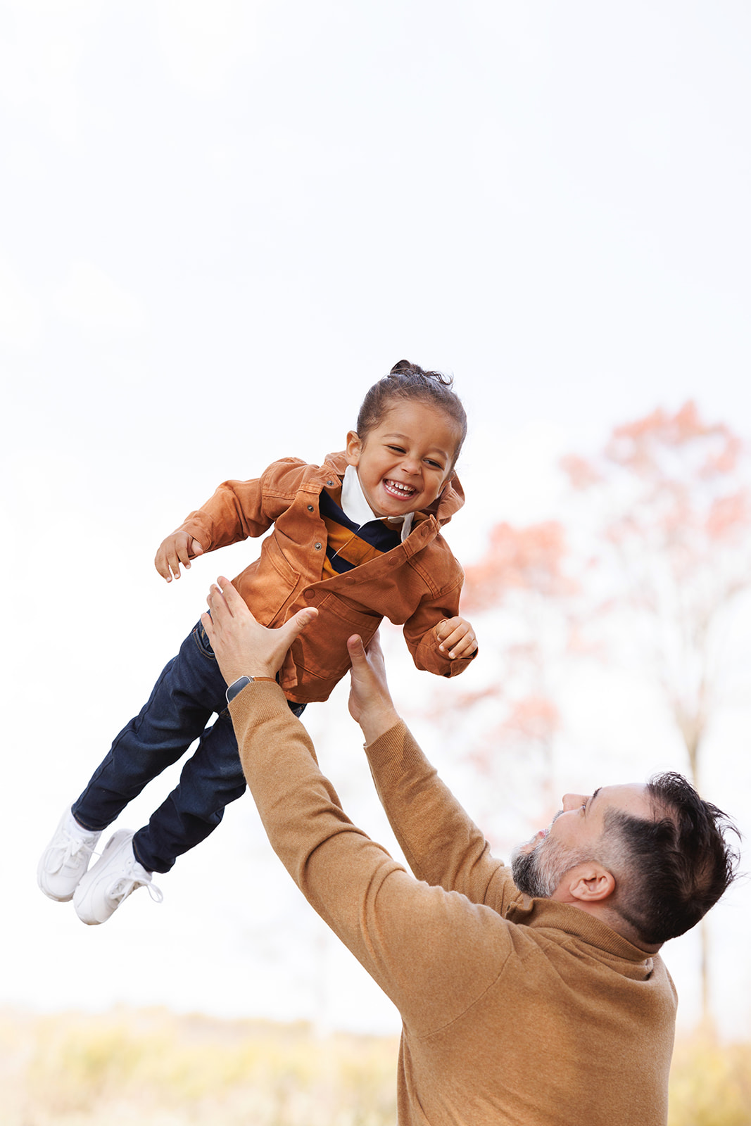 A toddler girl in an orange jacket giggles while being tossed in the air by dad in a park after visiting birthday party places in Morgantown, WV