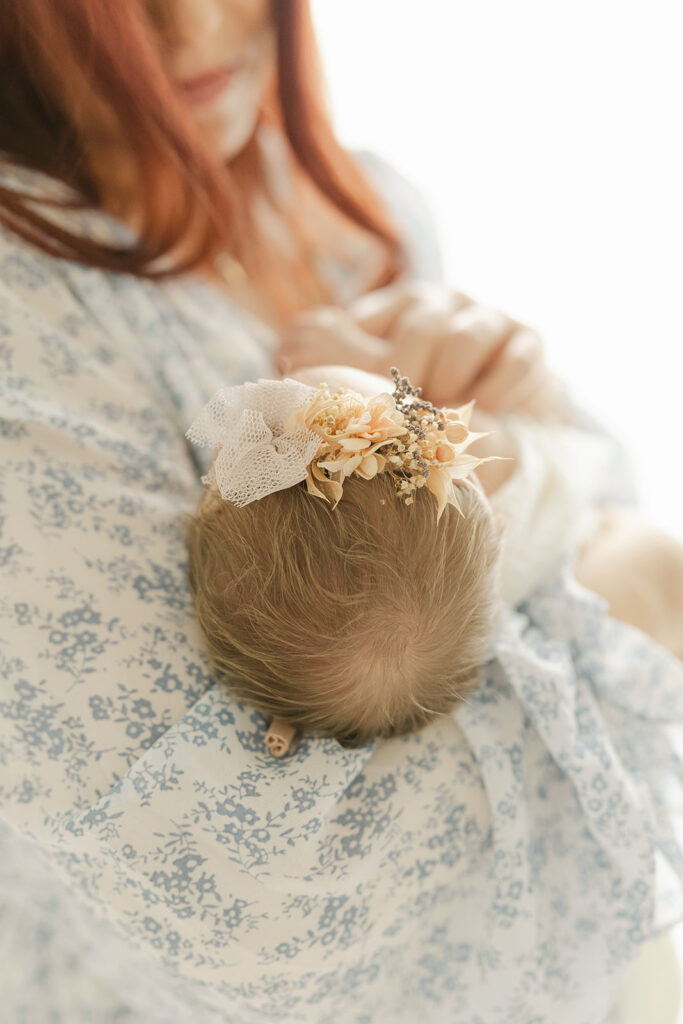 A newborn baby's head laying in mom's arms in a studio and blue floral dress after meeting Breastfeeding for Busy Moms