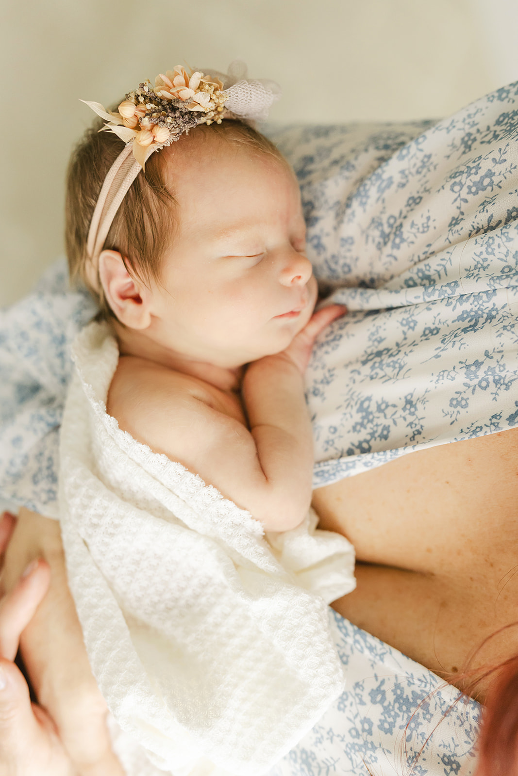 A newborn baby girl sleeps against mom's chest in a floral headband after meeting with Breastfeeding for Busy Moms