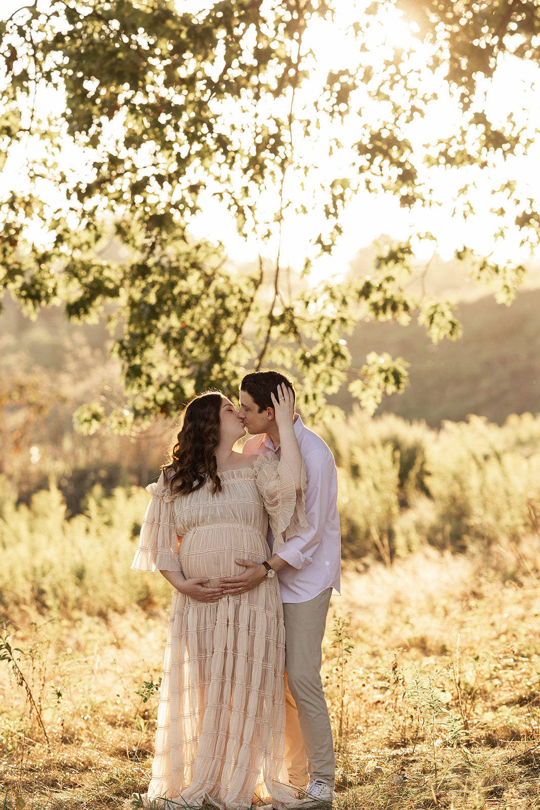 A happy expecting couple kisses under a tree at sunset thanks to a fertility clinic in Morgantown, WV