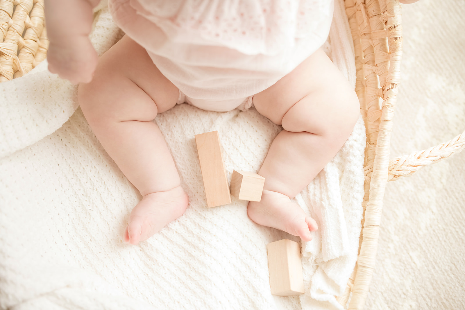 Details of a baby's legs in a woven basket with wooden toy blocks