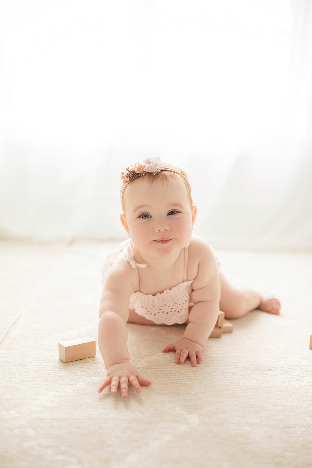 A happy baby girl crawls on the floor with wooden blocks under a window before visiting indoor playgrounds in Morgantown, WV