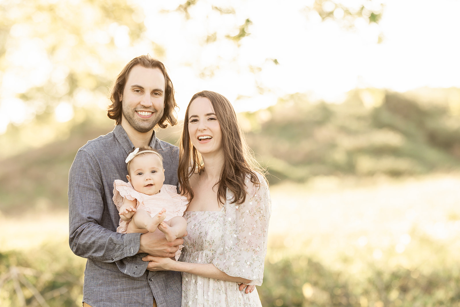 Happy mom and dad smile while holding their infant daughter in a park at sunset